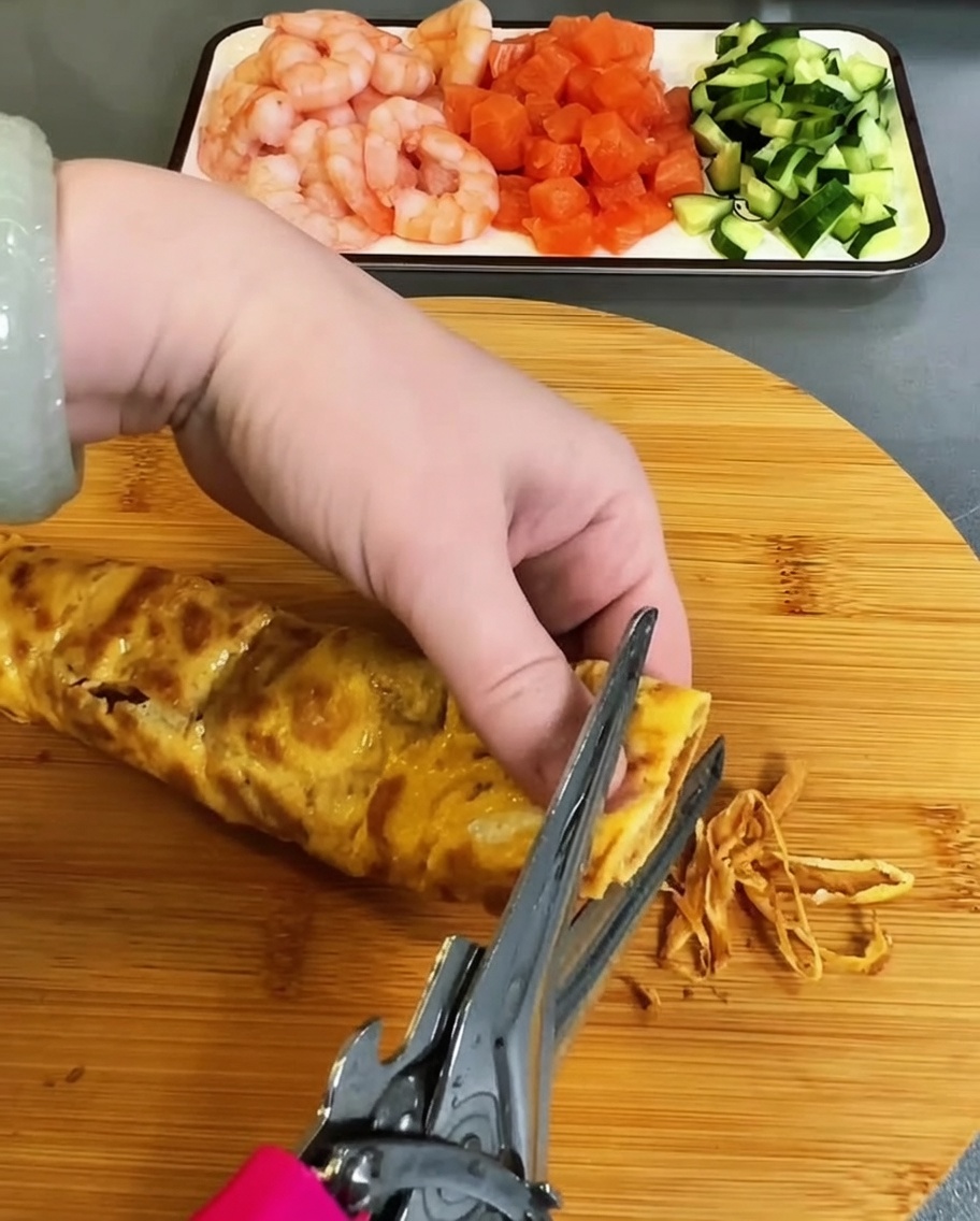 Tortilla de huevo cocida siendo cortada cuidadosamente en tiras finas con tijeras de cocina.