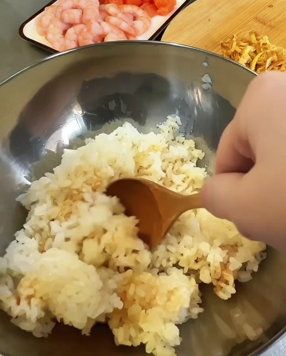 Arroz cocido siendo condimentado con vinagre y salsa de soja en un tazón de metal.