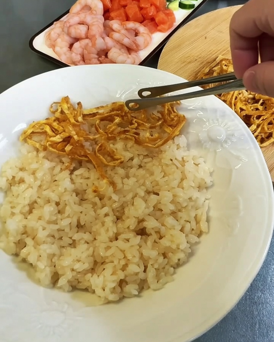 Distribución de coloridas tiras de huevo y mariscos sobre una cama de arroz condimentado en un plato blanco.