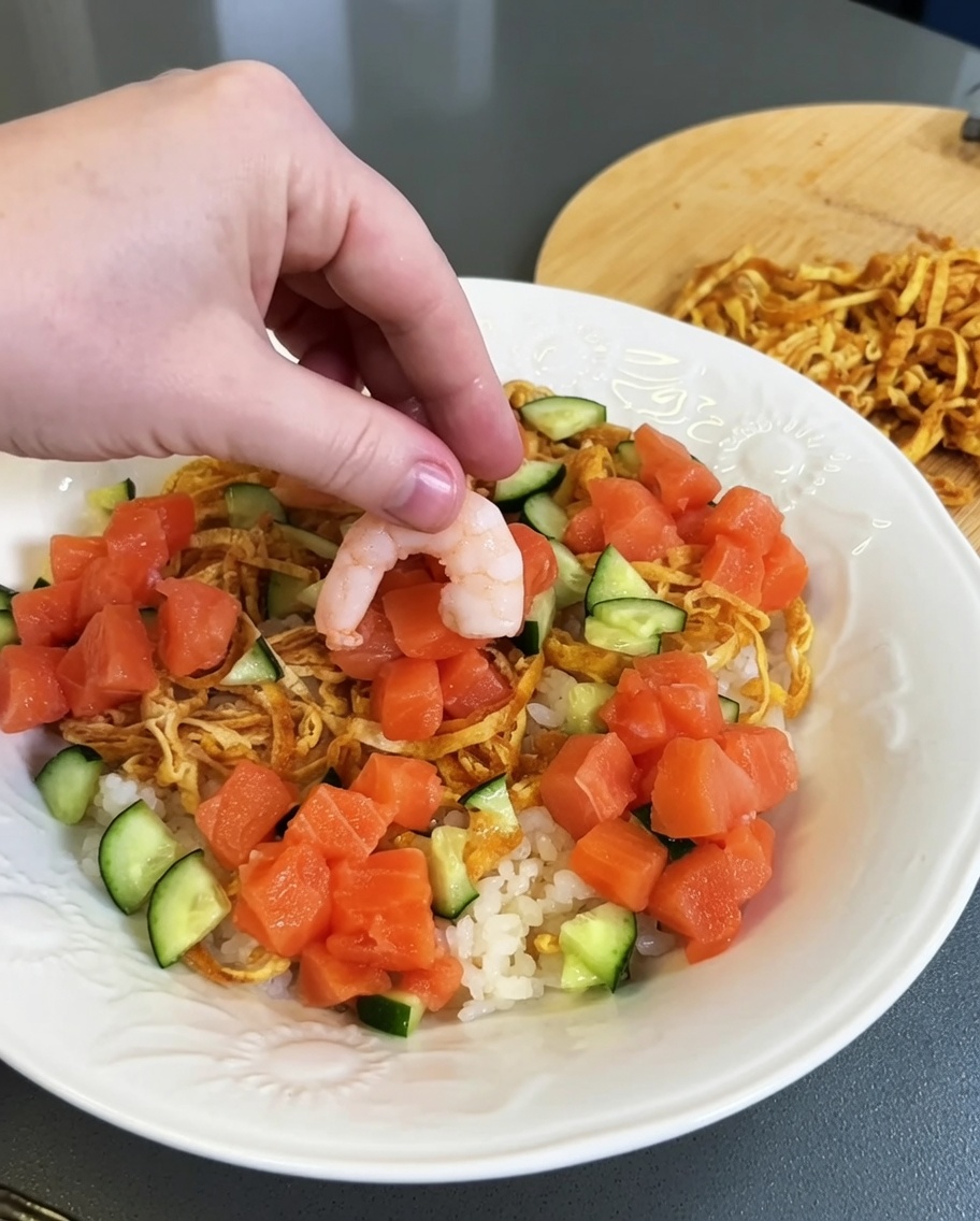 Grupos de salmón crudo fresco en dados siendo colocados en el plato de arroz preparado.