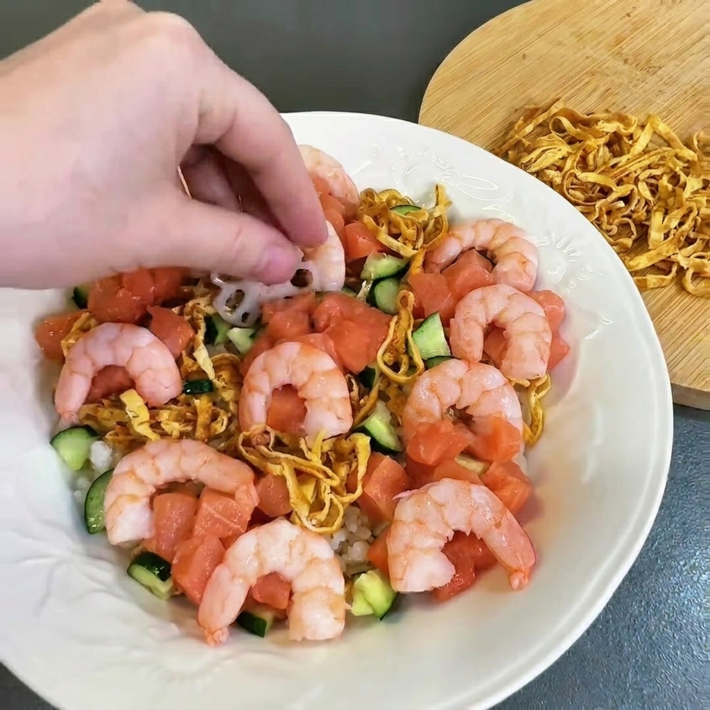 Camarones rosados cocidos siendo arreglados cuidadosamente en el plato lleno de salmón y pepino.
