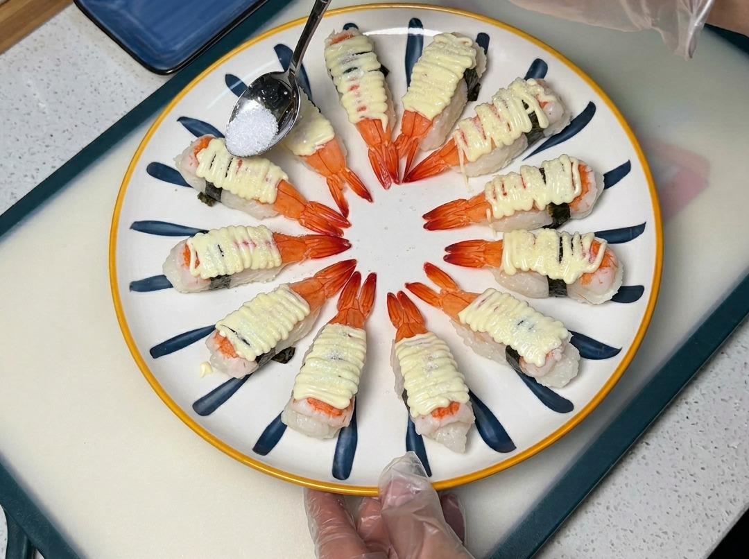 Una cuchara espolvoreando azúcar sobre el sushi de langostino con mayonesa en un plato decorativo.