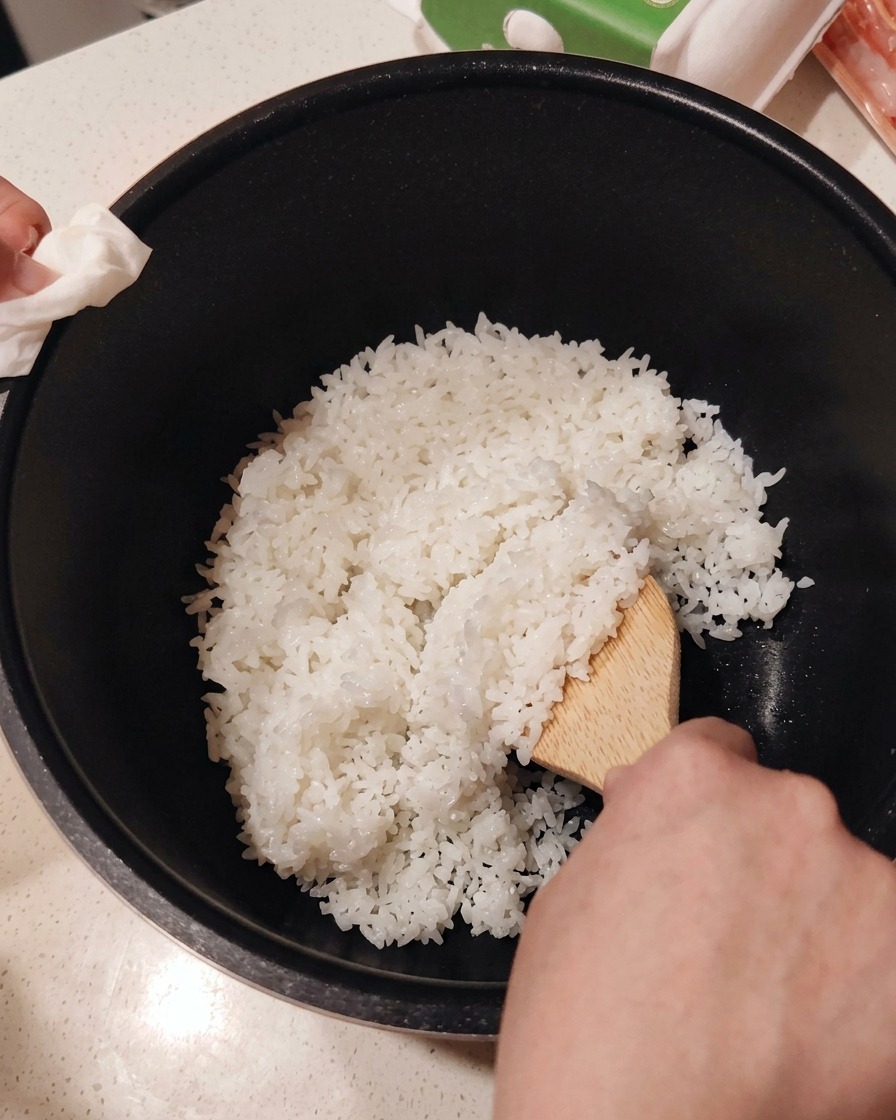Mezclando vinagre de sushi en arroz blanco recién cocido usando una paleta de madera.