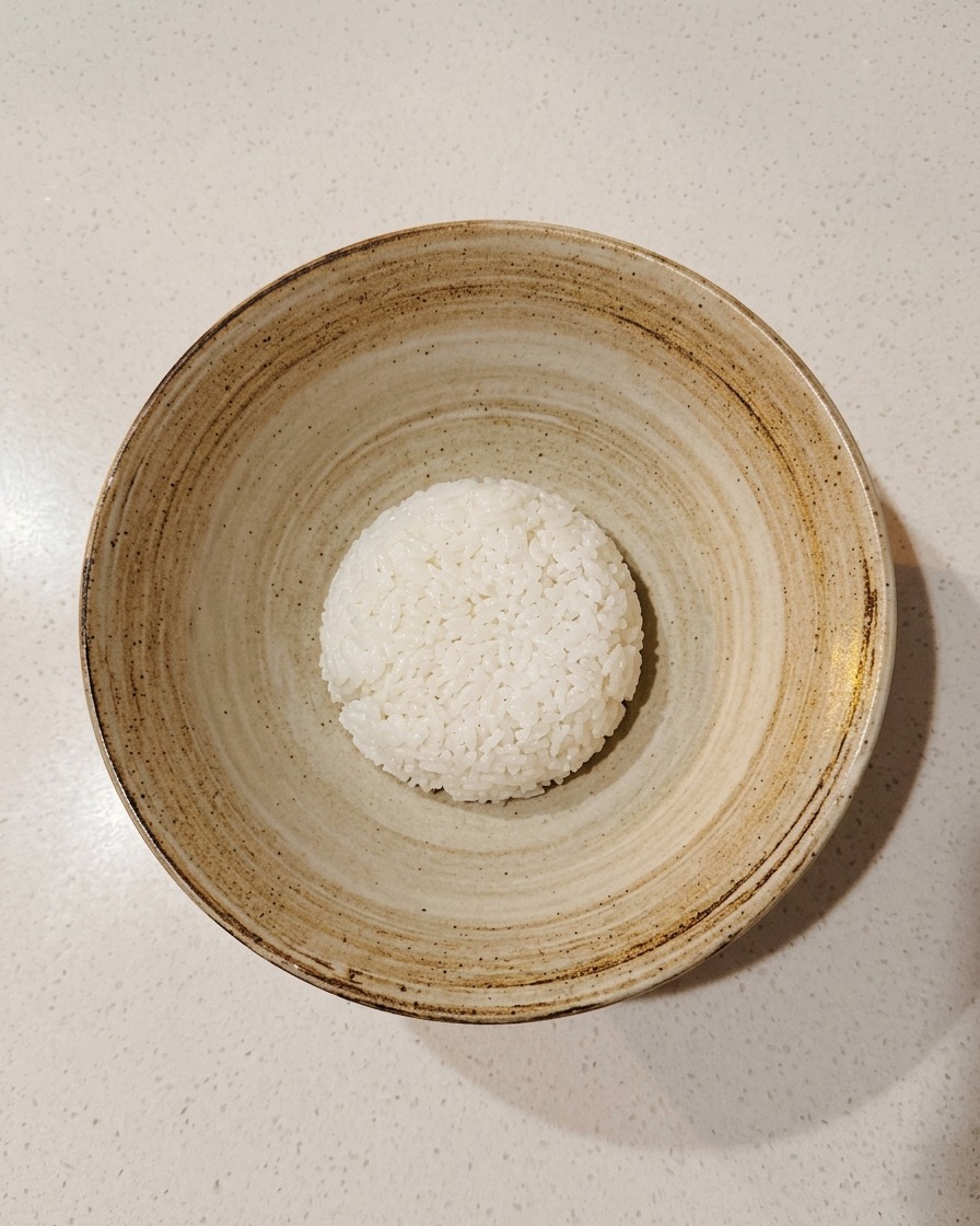 Una cucharada de arroz para sushi sazonado en el centro de un tazón rústico de cerámica.