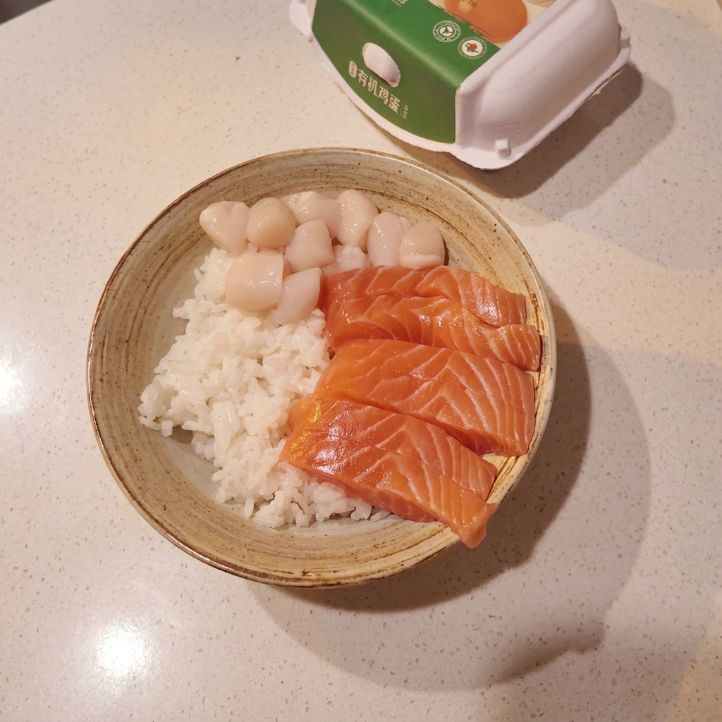 Un tazón con arroz, salmón, vieiras y camarones dulces.