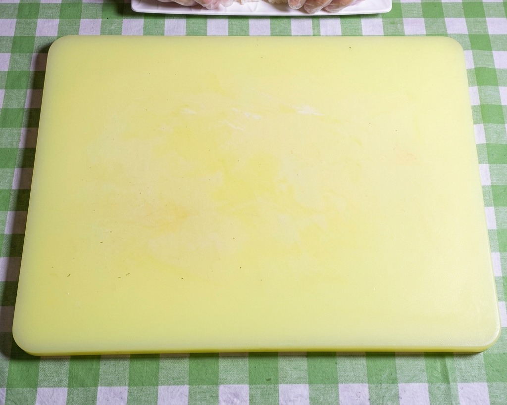 Primer plano de manos con guantes dando forma a arroz pegajoso en bolas ovaladas uniformes sobre una tabla amarilla.