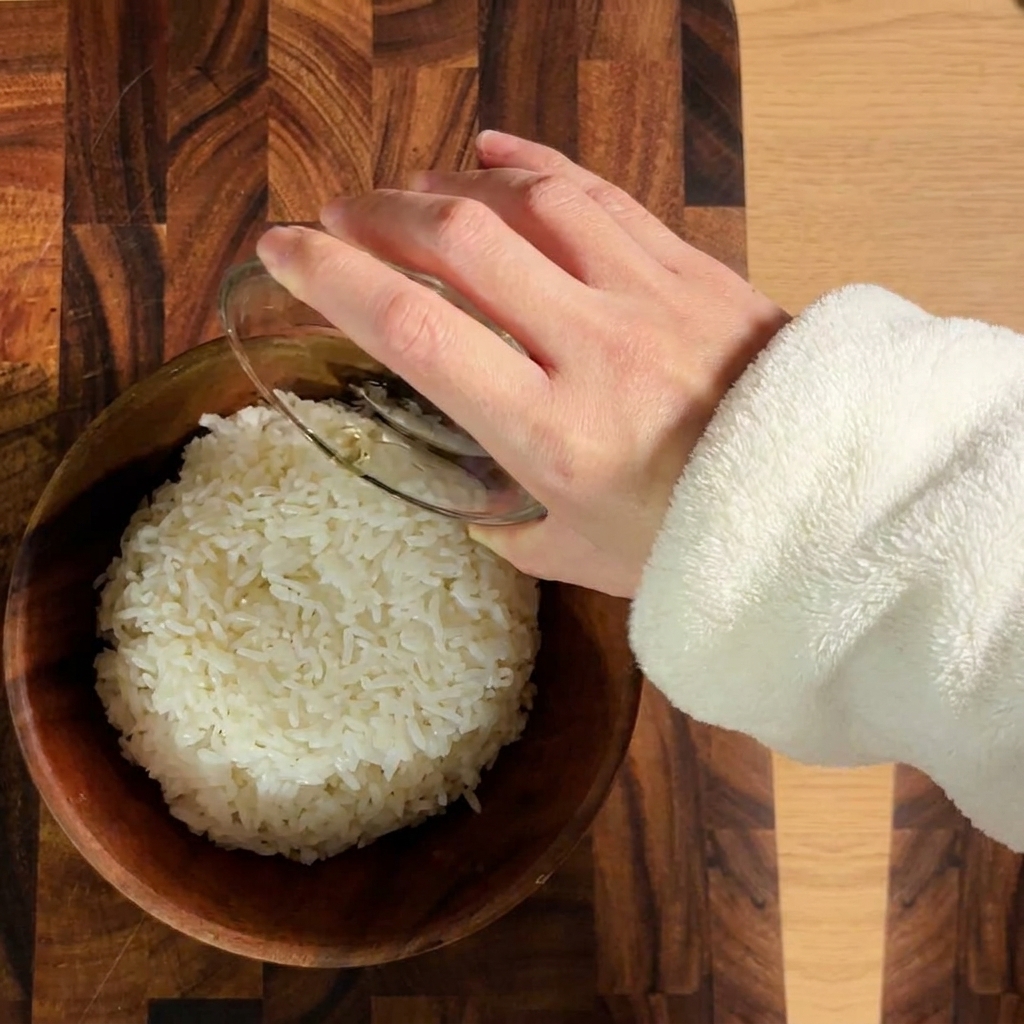 Arroz blanco cocido siendo sazonado con vinagre de sushi en un tazón de madera.