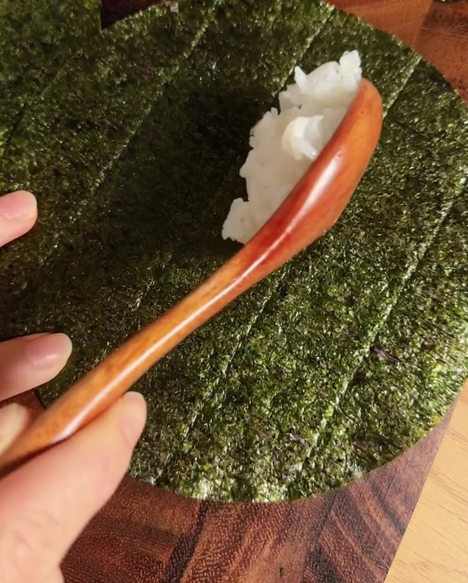 Una línea de arroz para sushi sazonado centrada en una hoja circular de nori.