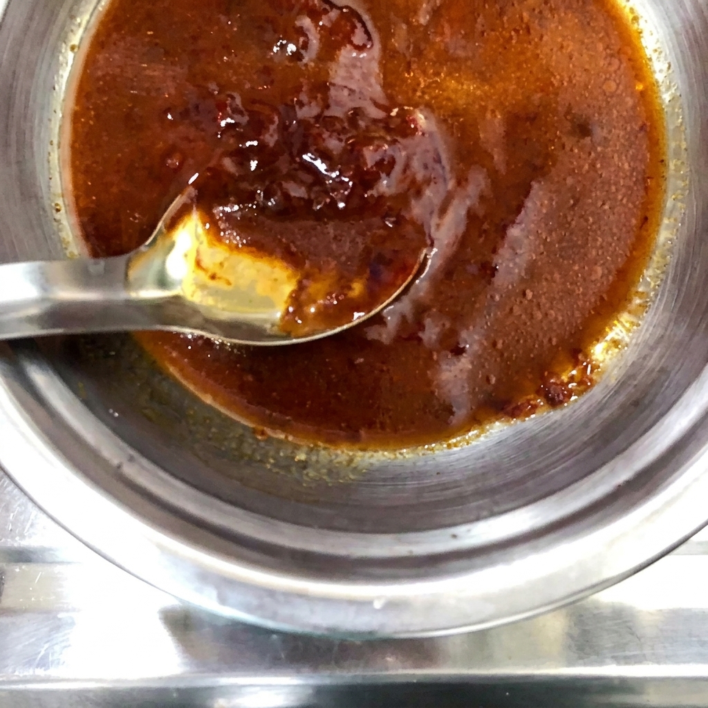 Un polvo de especias seco siendo espolvoreado sobre la mezcla de salsa preparada en el bol metálico.