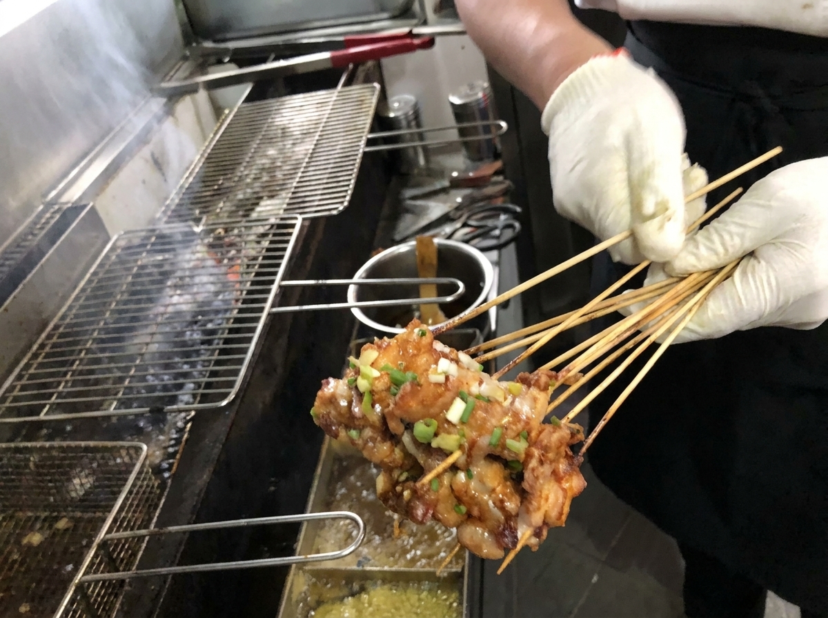 Primer plano de un pincel aplicando una rica salsa marrón sobre brochetas de panceta asadas al dorado en una parrilla de carbón.