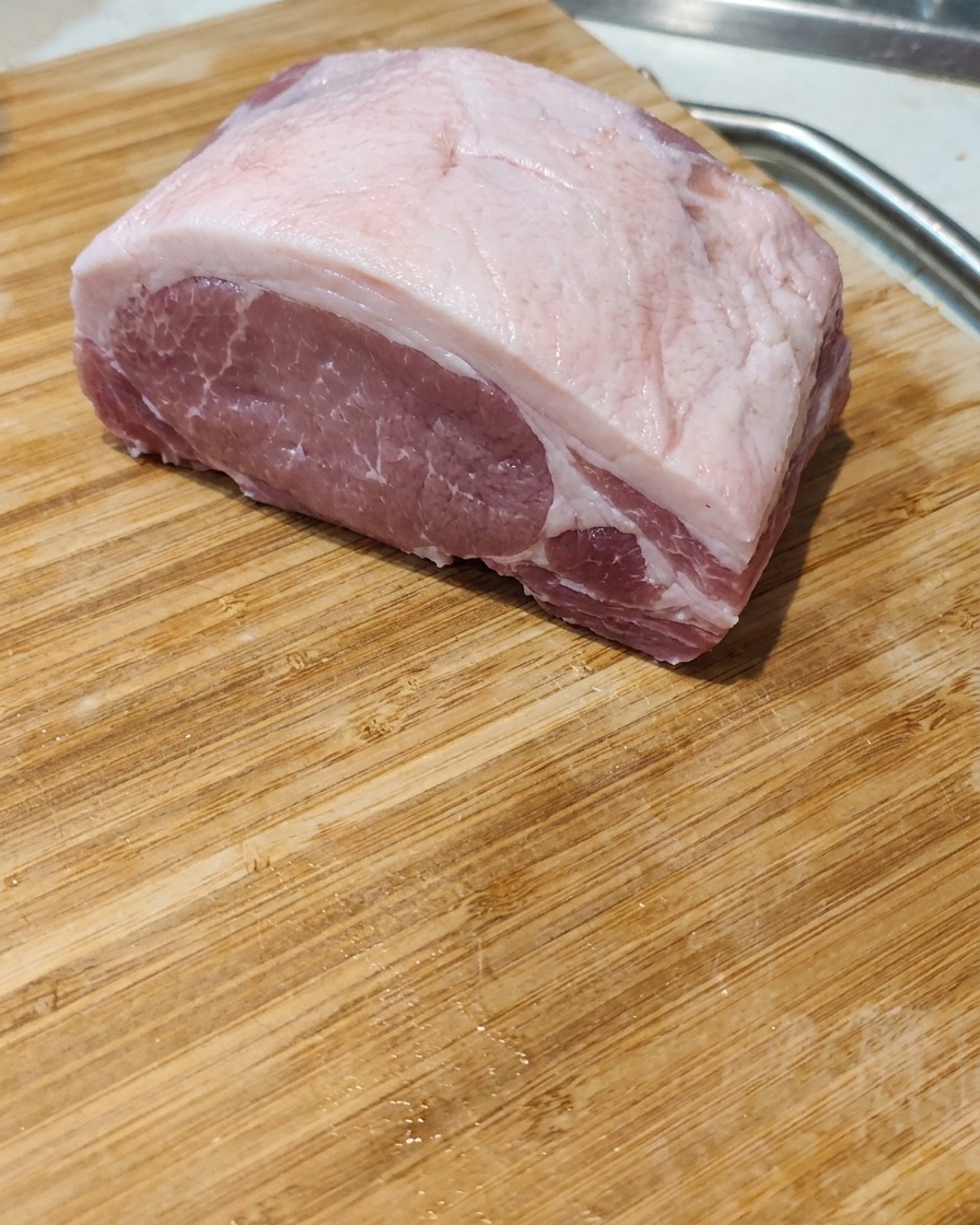 Primer plano de un bloque de panceta de cerdo cruda siendo cortado en porciones gruesas y uniformes sobre una tabla de madera.