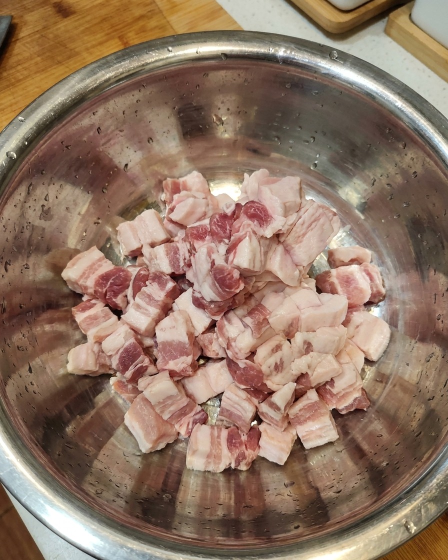 Rebanadas de panceta de cerdo cruda reunidas en un tazón grande de acero inoxidable.