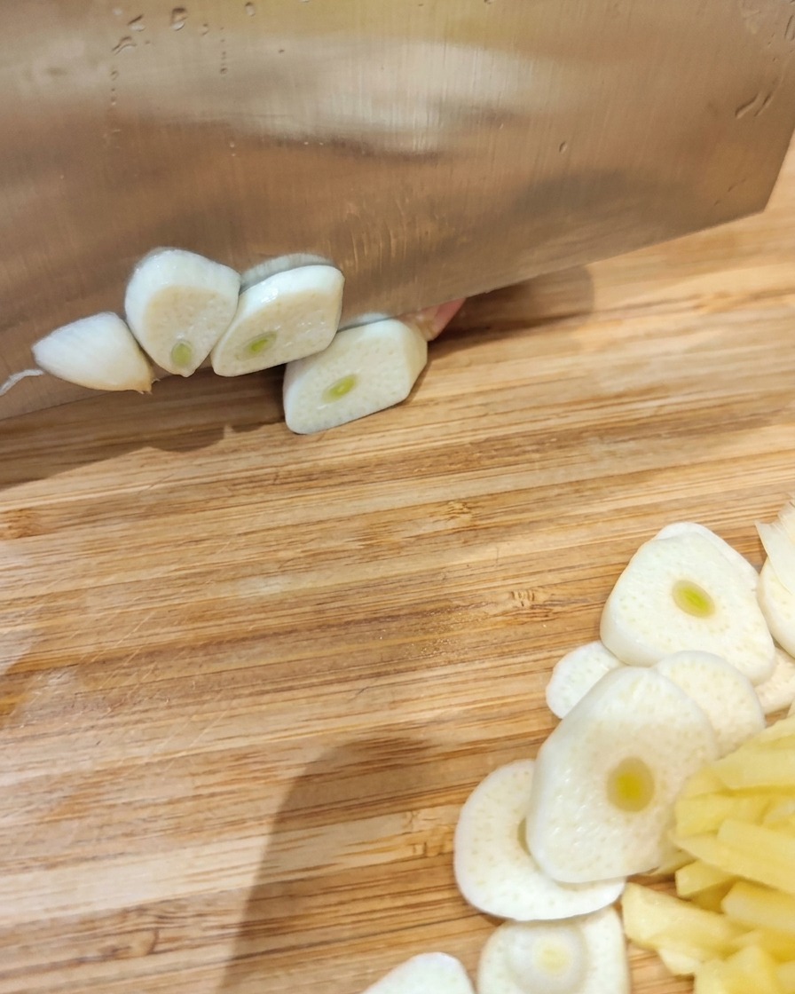 Panceta de cerdo cruda en un tazón cubierta con láminas de ajo, jengibre y varios polvos de especias.