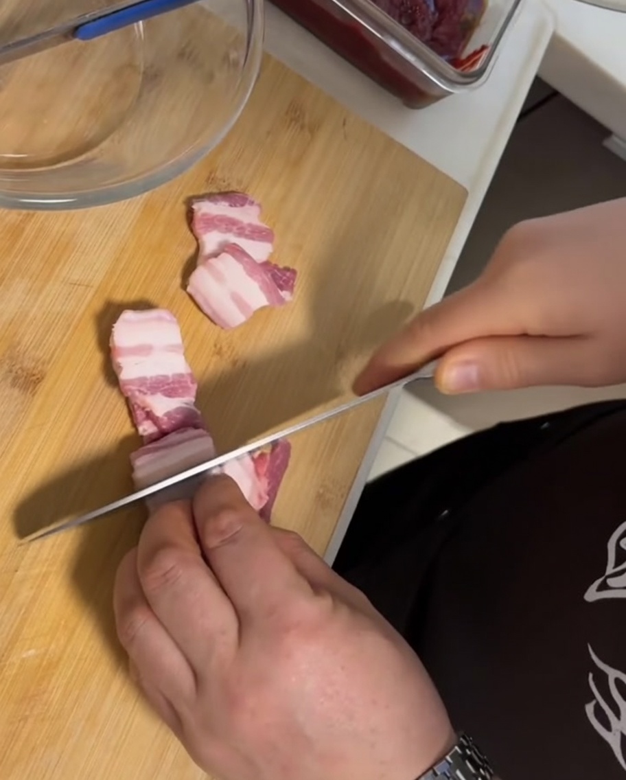 Gruesas rebanadas de panceta de cerdo cruda con piel sobre una tabla de cortar de madera junto a un cuchillo.