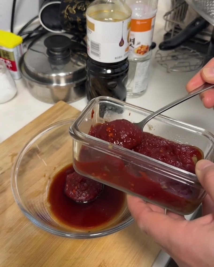 Una salsa espesa de color rojo oscuro siendo mezclada con una cuchara en un tazón de vidrio sobre una superficie de madera.