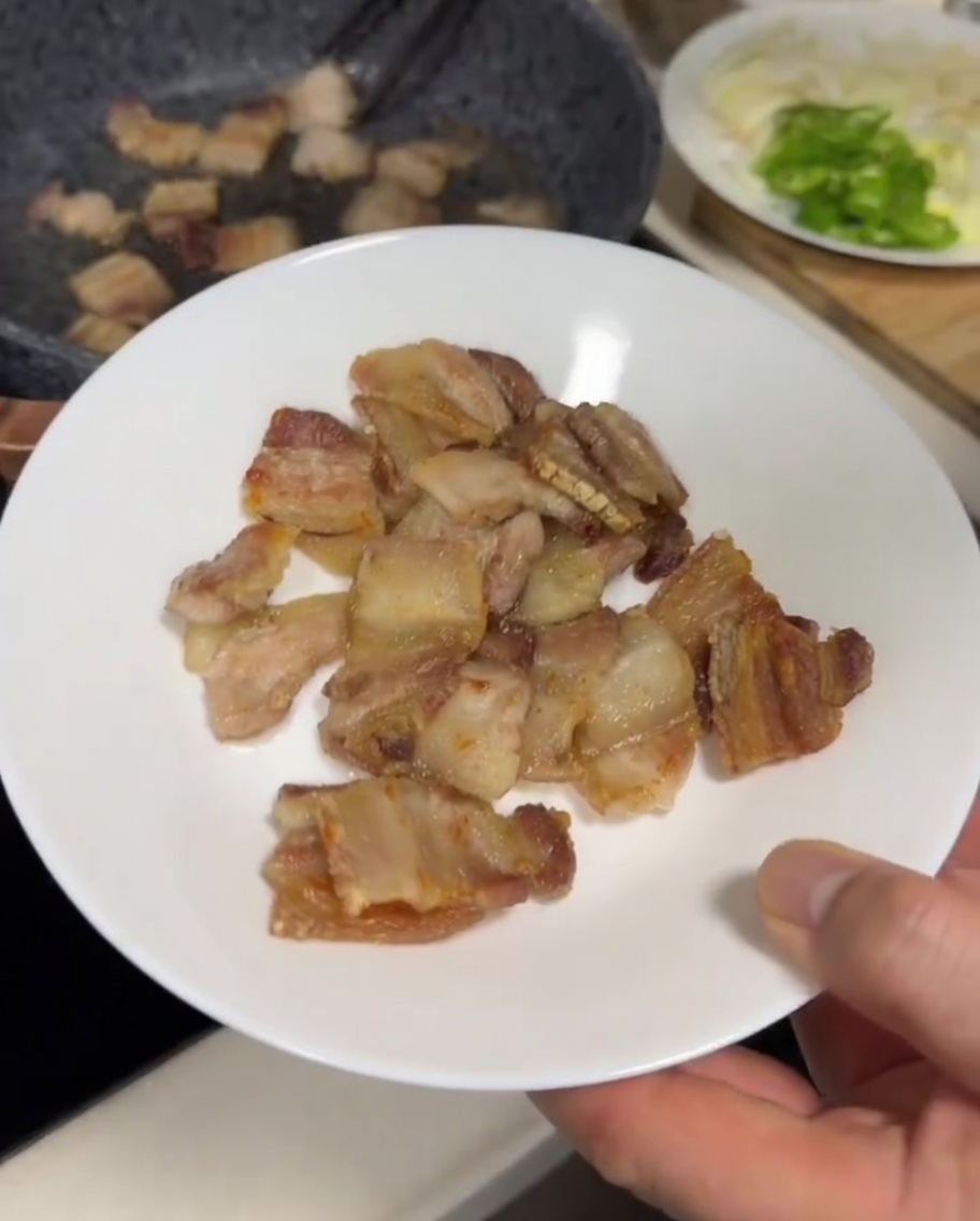 Láminas de panceta friéndose en una sartén gris, con un exterior dorado y ligeramente crujiente.