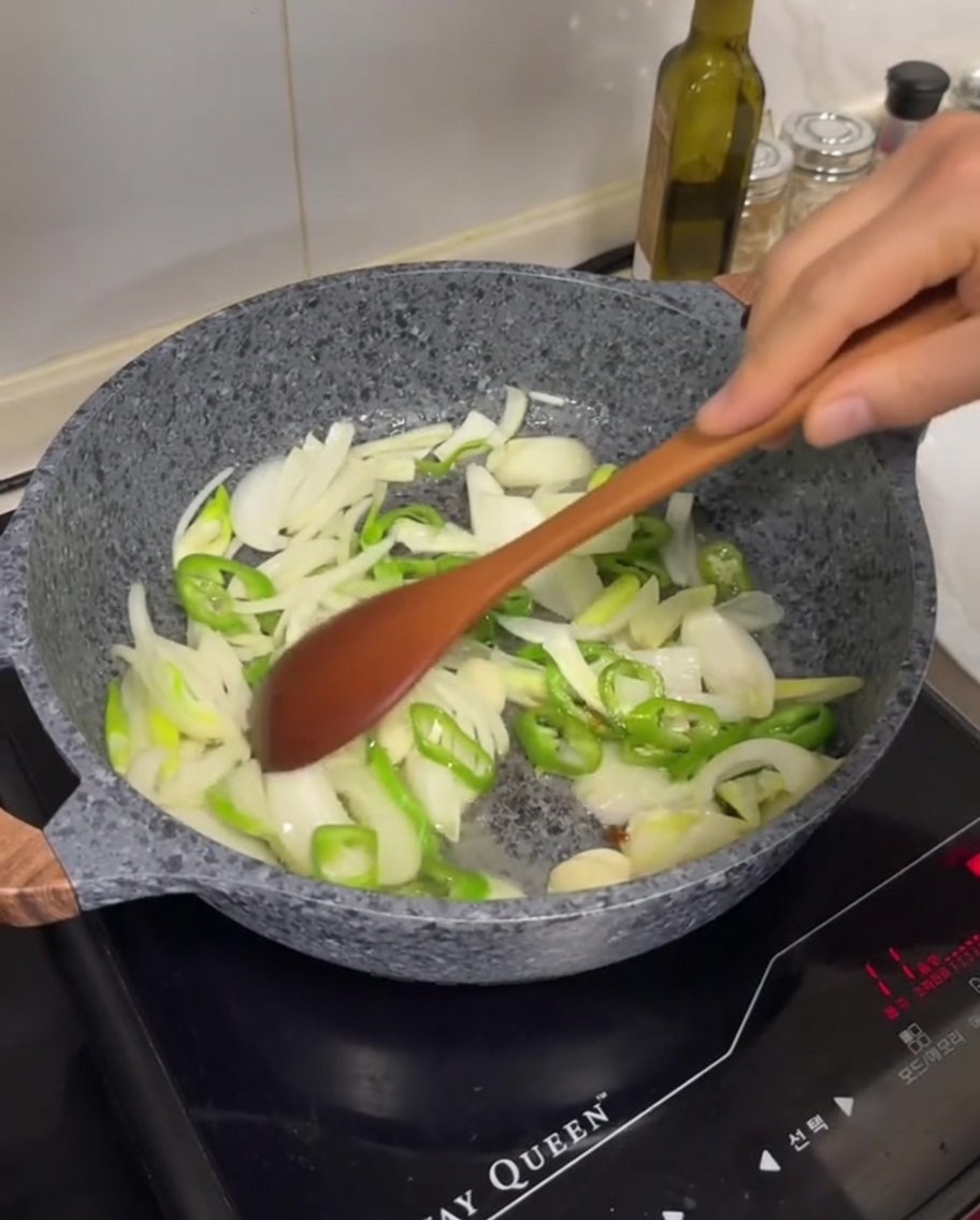 Cebolla blanca en rodajas, chiles verdes y dientes de ajo siendo salteados en una sartén con la grasa del cerdo.