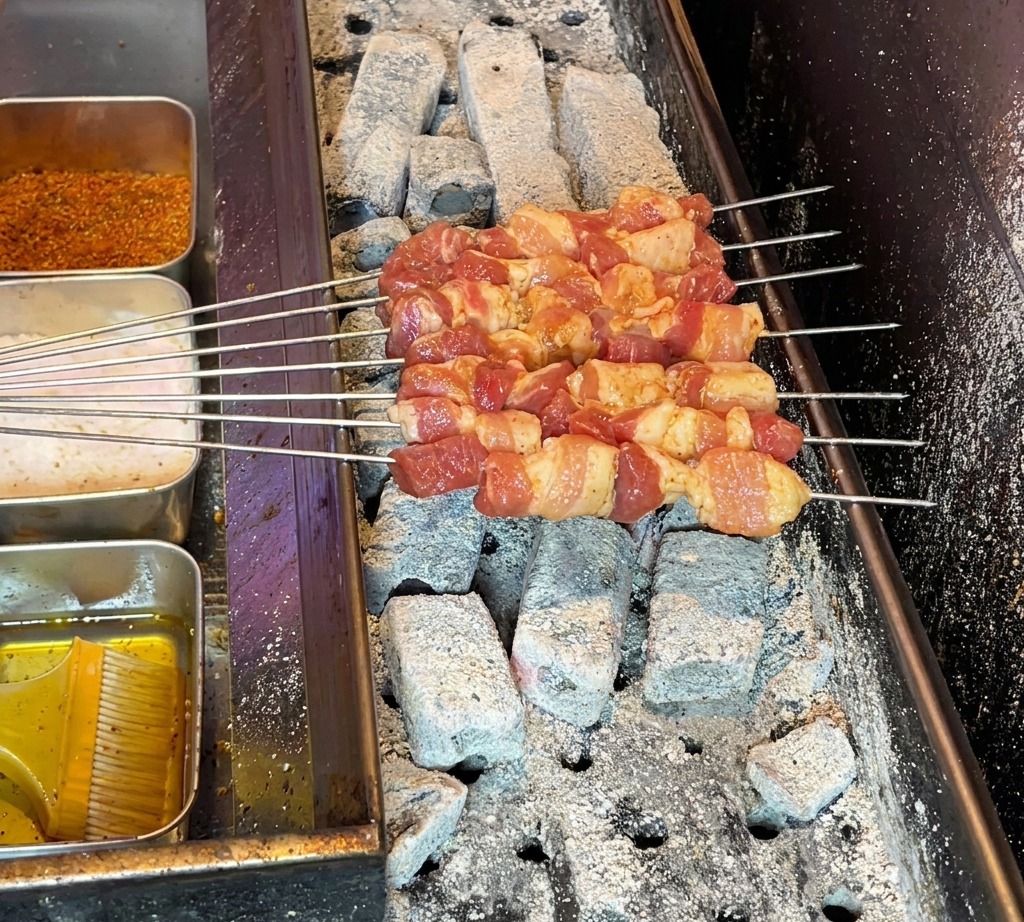 Brochetas de panceta de cerdo cruda dispuestas en una parrilla de carbón caliente, listas para empezar a cocinar.