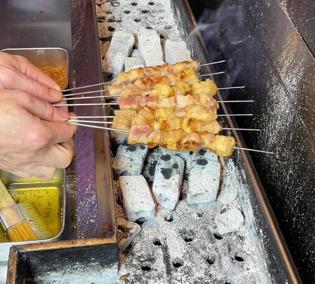 Manos del chef manipulando cuidadosamente las brochetas para asegurar una distribución uniforme de la grasa sobre la carne cocinándose.