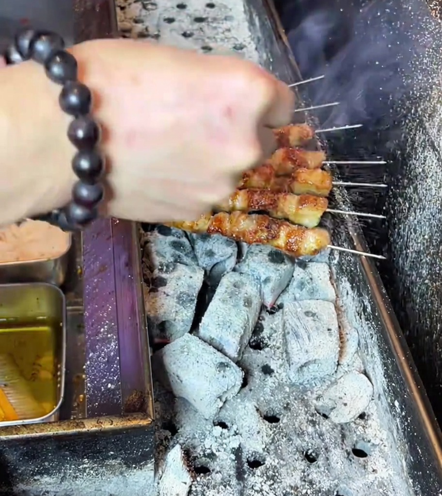 Mano espolvoreando polvo de sazonador sobre brochetas de panceta de cerdo perfectamente asadas y doradas en la parrilla de carbón.