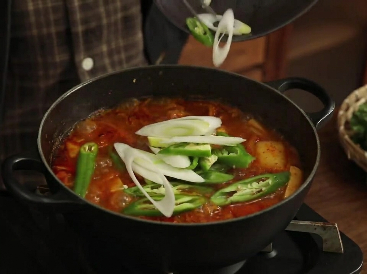 Rodajas de pimiento verde y puerros siendo añadidos al estofado burbujeante.