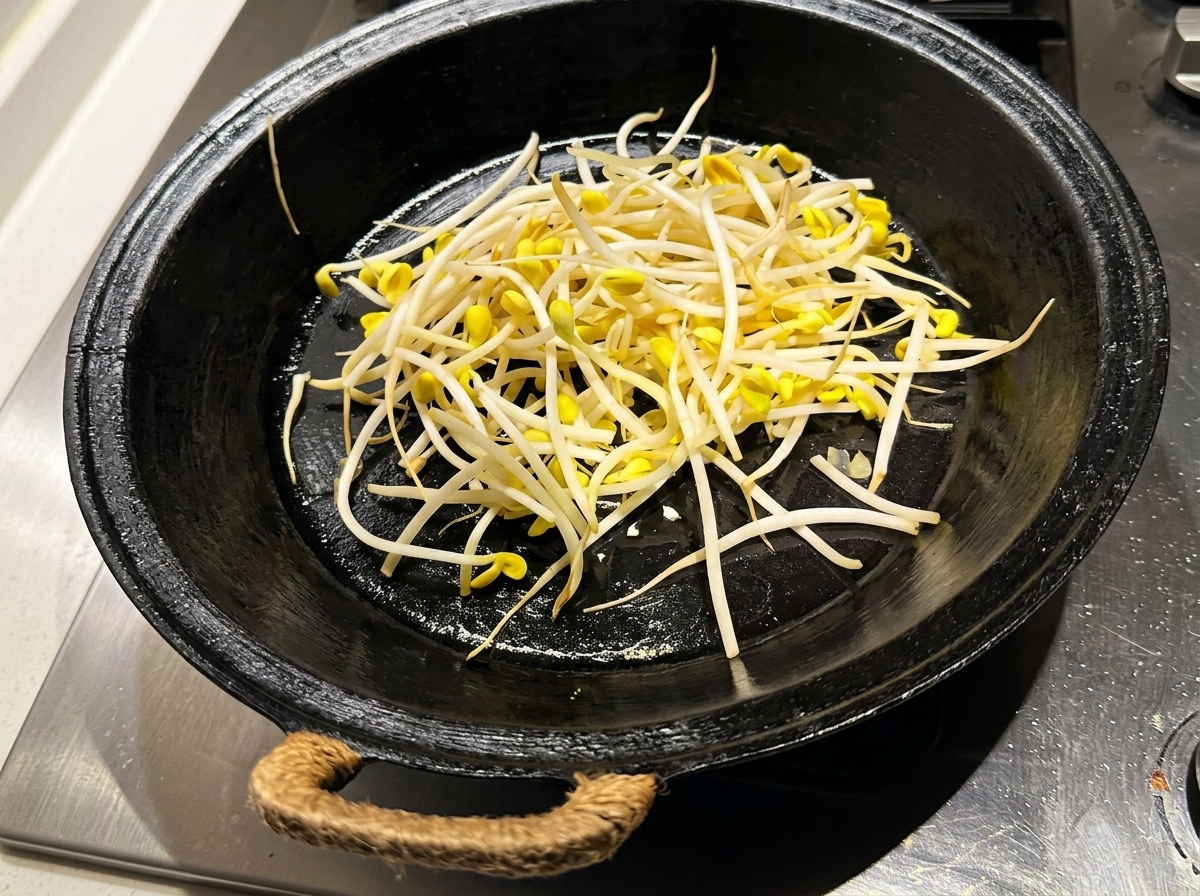 Brotes de soja frescos y limpios extendiéndose en una sartén negra precalentada y aceitada.