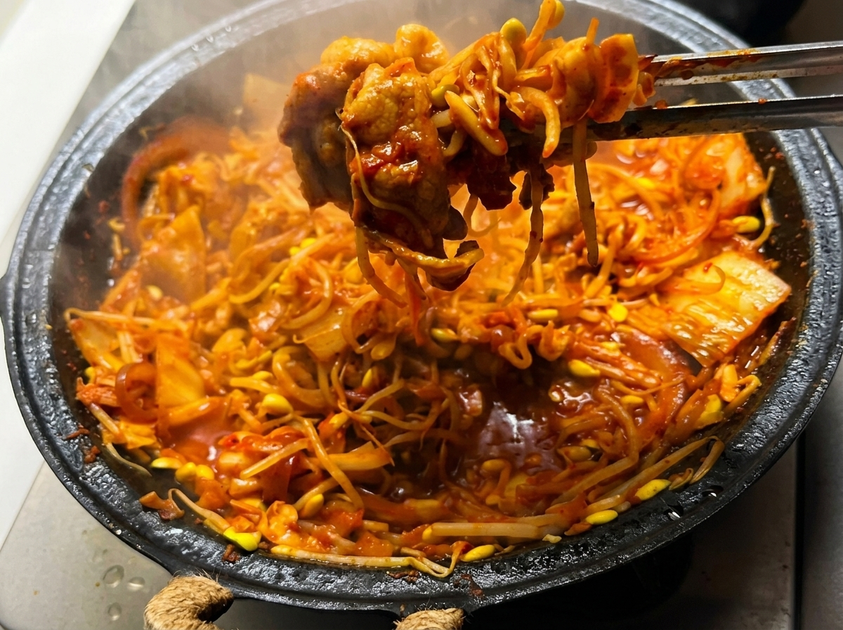 La mezcla de panceta con kimchi y brotes de soja siendo removida en la sartén sobre una llama alta.