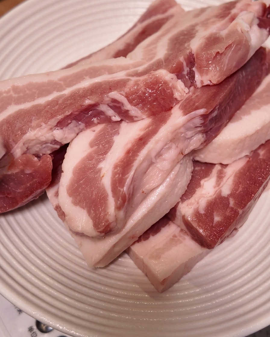 Rodajas gruesas de panceta cruda apiladas en un plato blanco estriado.