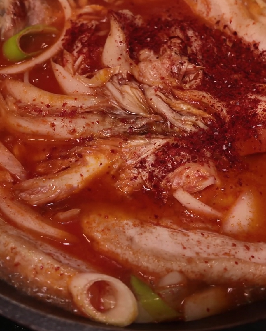 Chili en polvo rojo espolvoreado sobre la carne, el kimchi y las cebollas en la sartén.