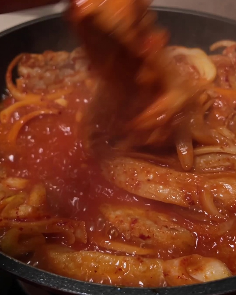 Los ingredientes siendo removidos juntos en la salsa roja burbujeante en la sartén.
