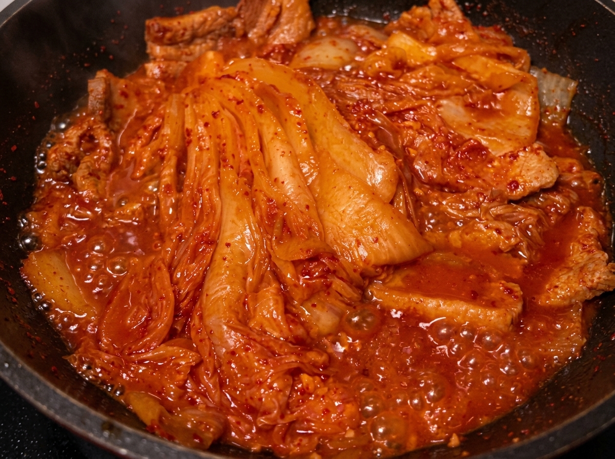 Aceite siendo vertido desde una cuchara en la sartén con el cerdo y el kimchi braseados.