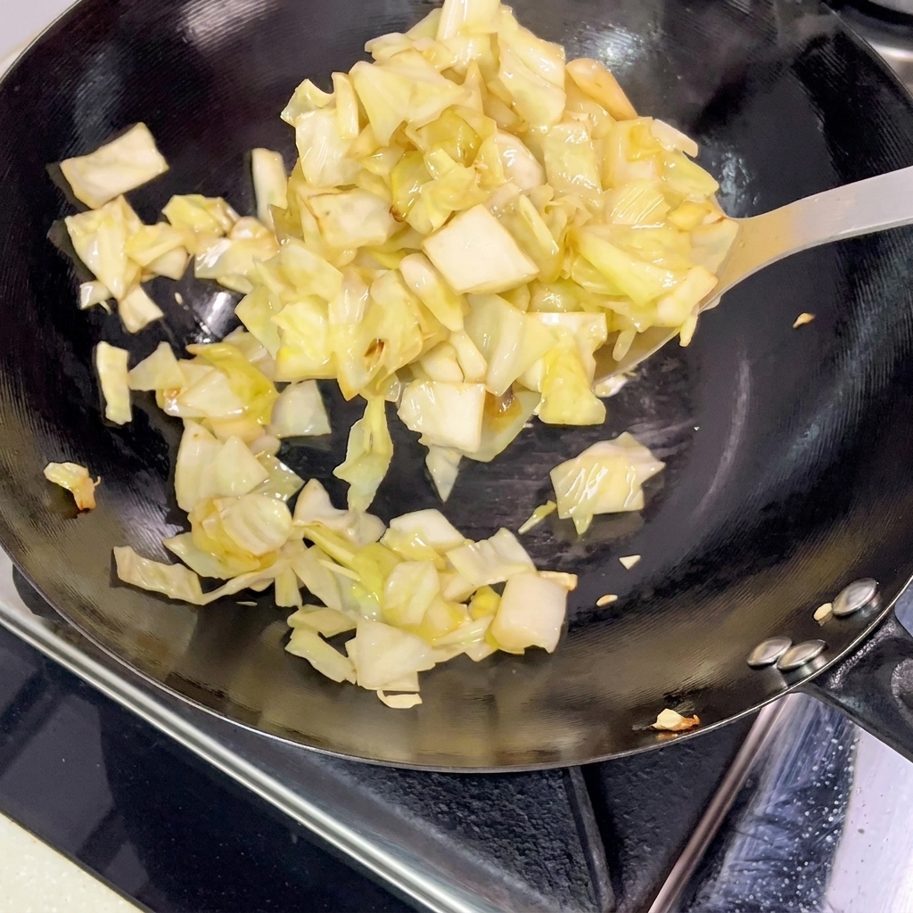 Trozos de col encurtida siendo retirados de un wok caliente con una espátula de metal.