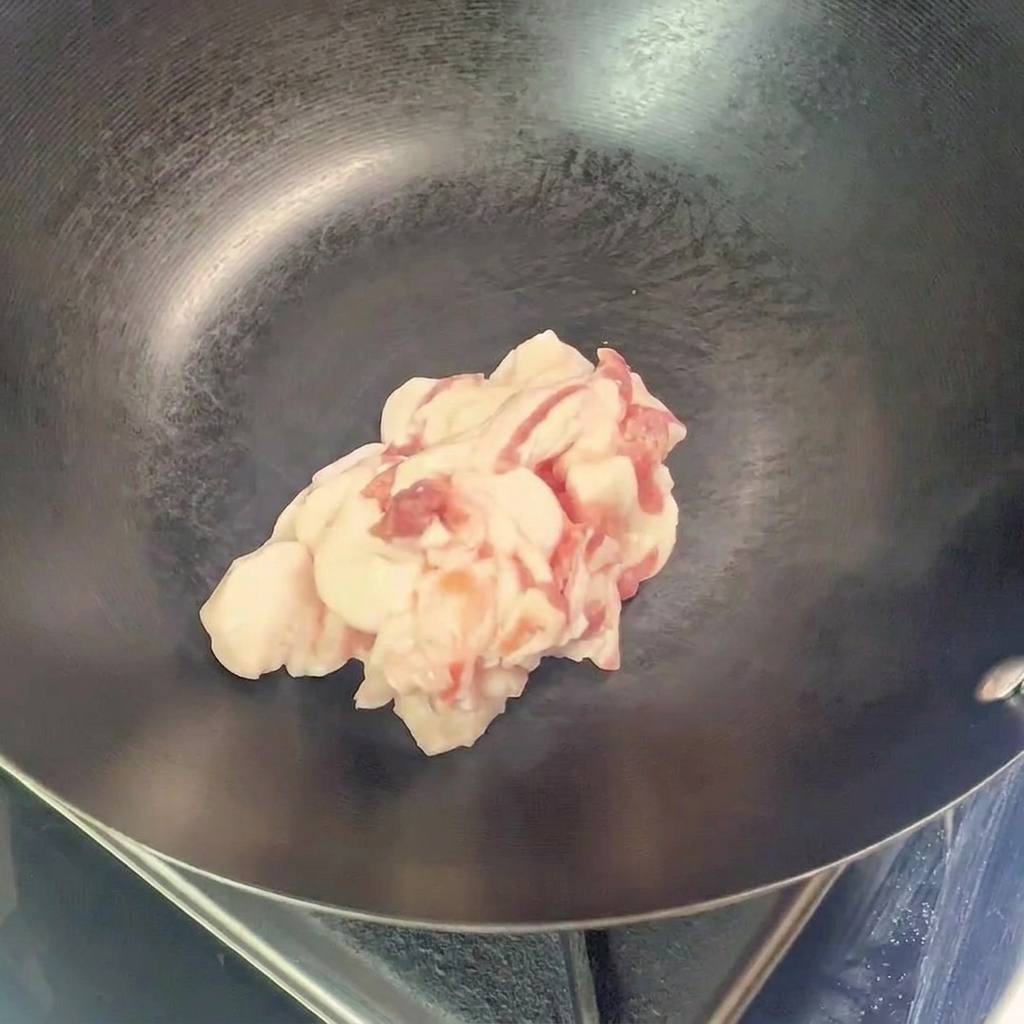 Un montón de trozos de panceta de cerdo cruda, cortada en láminas, colocados en el centro de un wok vacío precalentado.
