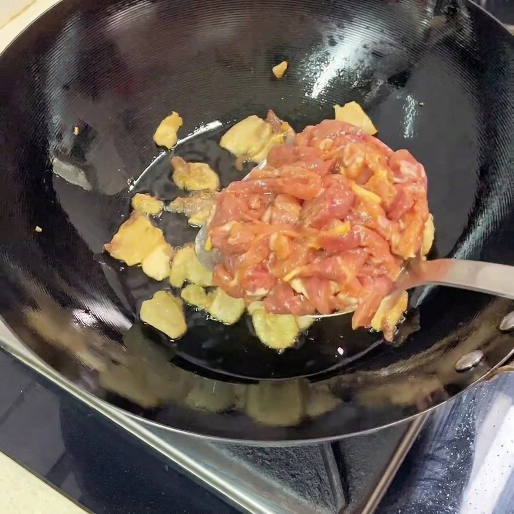 Tiras de cerdo magro marinado siendo añadidas al wok caliente con la panceta de cerdo fundida.