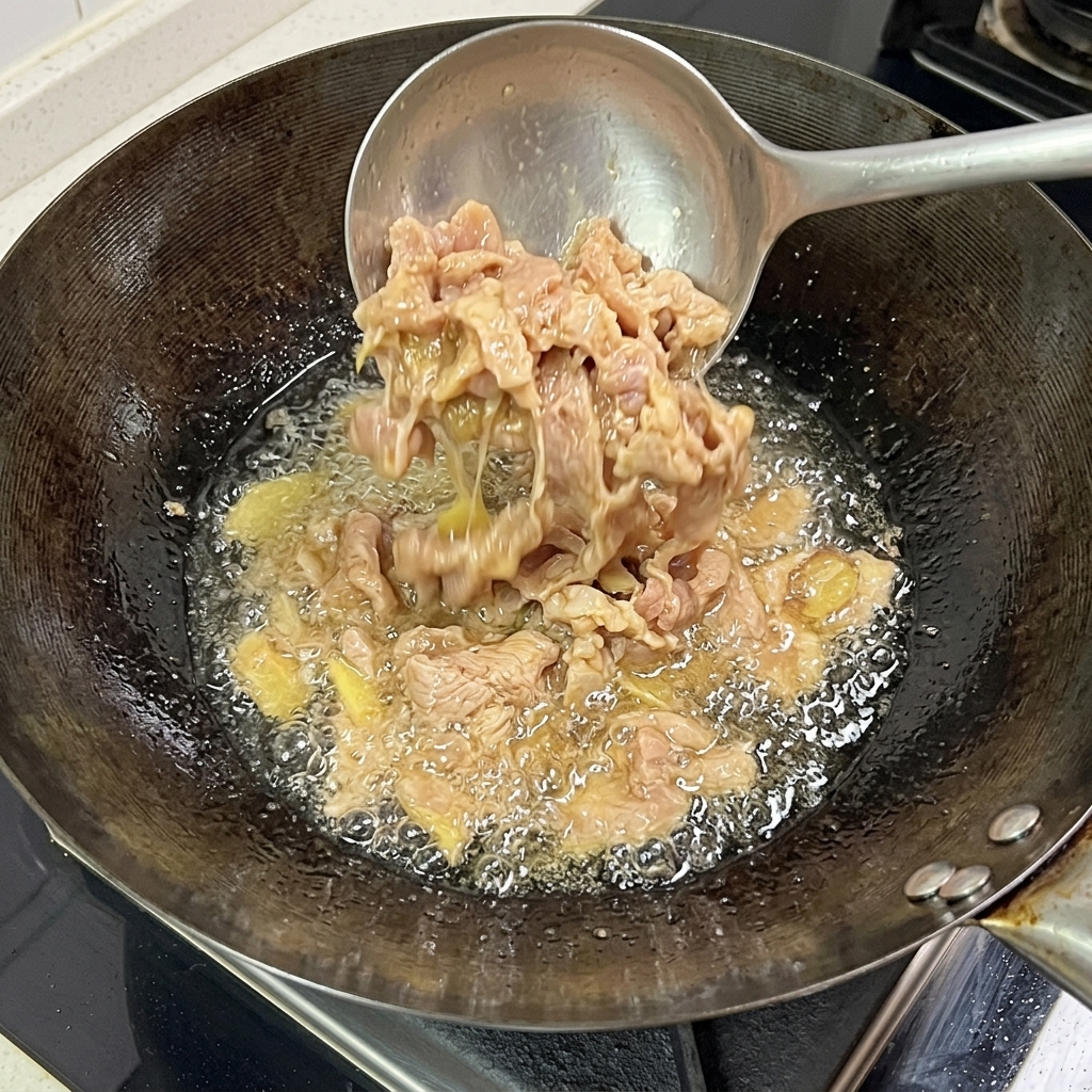 Láminas de cerdo friéndose en el wok, mostrando una superficie exterior cocinada y dorada.