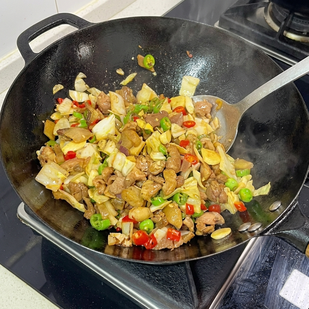 Una espátula de metal removiendo activamente col encurtida, cerdo laminado y chiles picados juntos en un wok humeante.