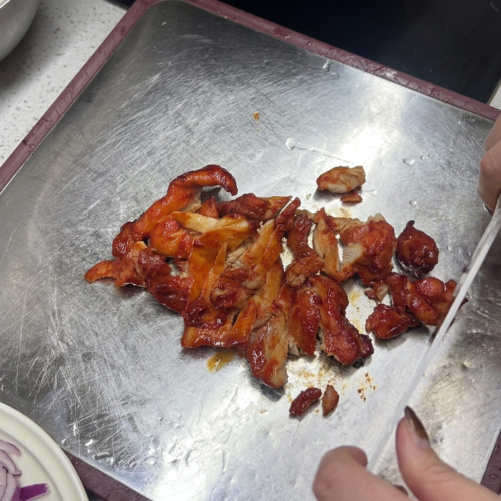Un cuchillo rebanando pollo glaseado y cocido de color marrón rojizo sobre una tabla de cortar metálica.