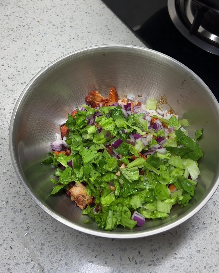 Primer plano de sal, comino en polvo y chile en polvo espolvoreándose sobre la mezcla de pollo, arroz y verduras frescas en un tazón de acero inoxidable.
