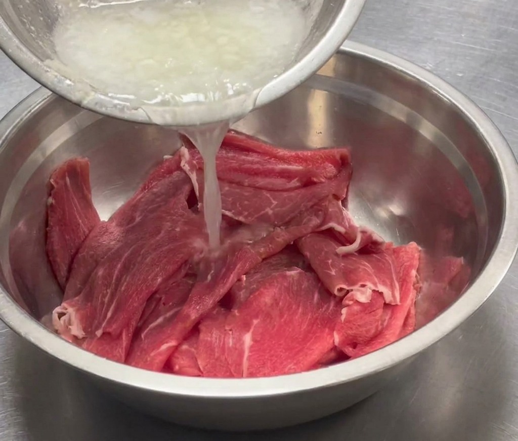 Puré aromático vertiéndose en un gran tazón de acero que contiene la carne en rodajas.