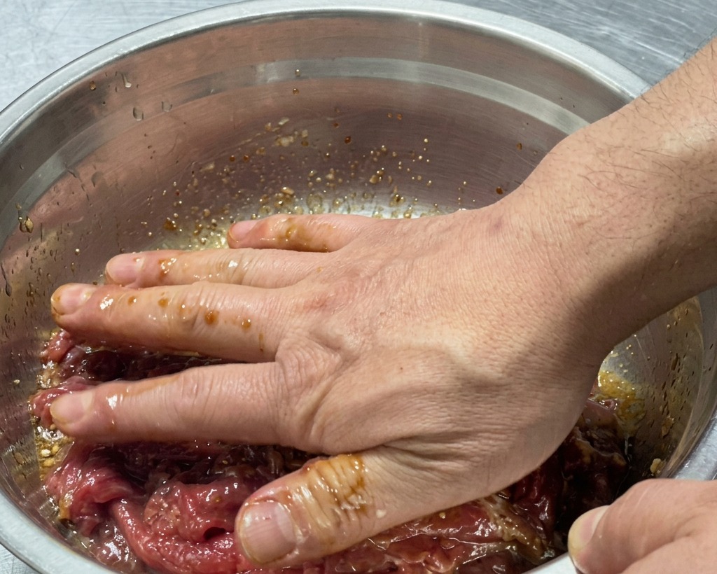 Manos mezclando a fondo la carne cruda con el adobo dentro del tazón.