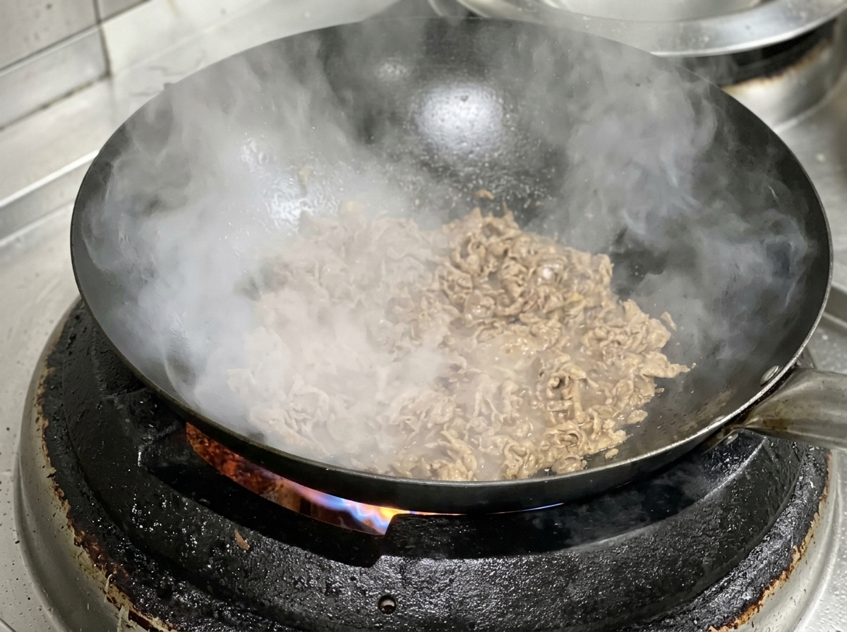 Rodajas de carne y cebolla cocinándose juntas en un wok caliente.