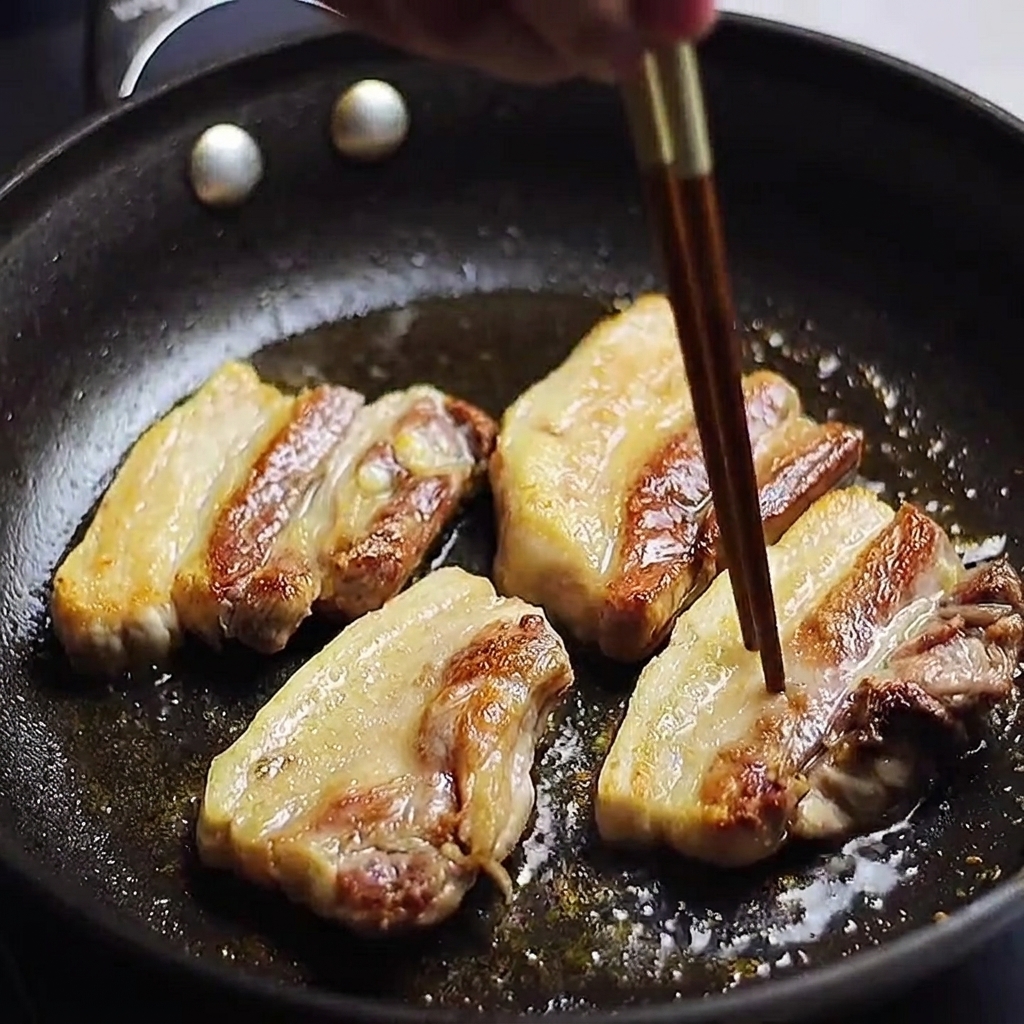 Tiras de panceta dorándose en una sartén, siendo verificadas con un palillo para ver si la carne está lista.