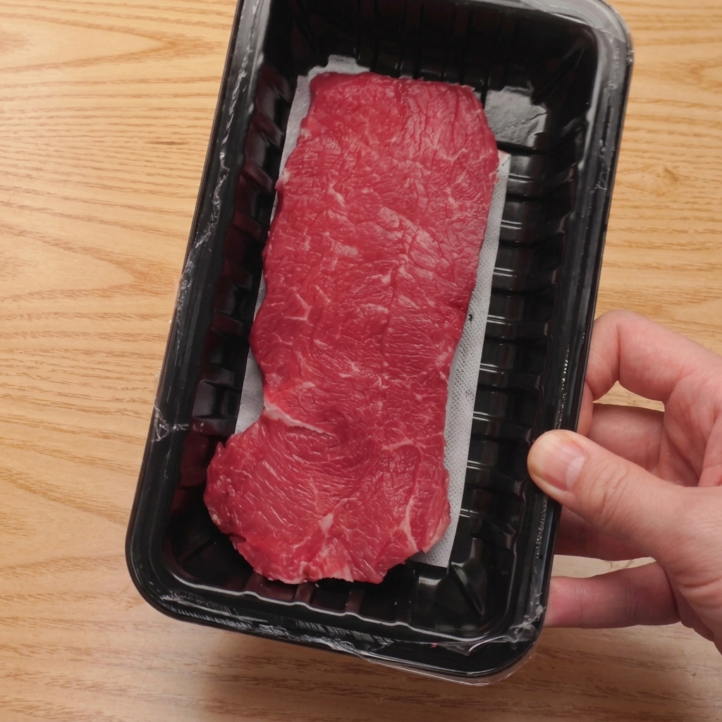 Solomillo de ternera crudo cortándose en cubos uniformes sobre una tabla de cortar de madera.