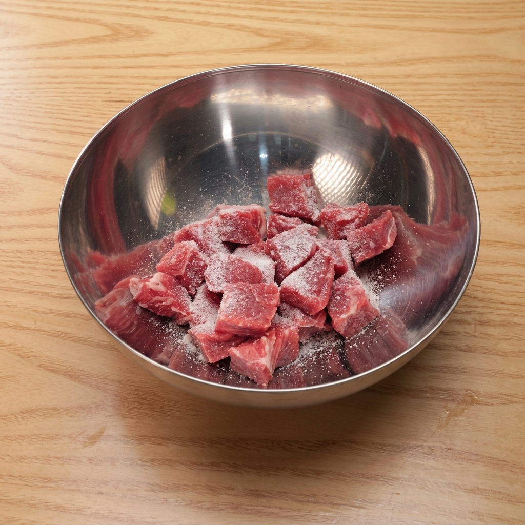 Cubos de ternera en un bol de mezcla metálico cubriéndose con sal, azúcar, salsa de soja y almidón.