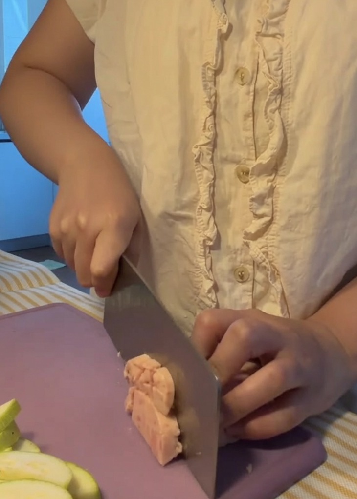 Carne de almuerzo siendo cortada en cubos pequeños y uniformes sobre una tabla de cortar morada.