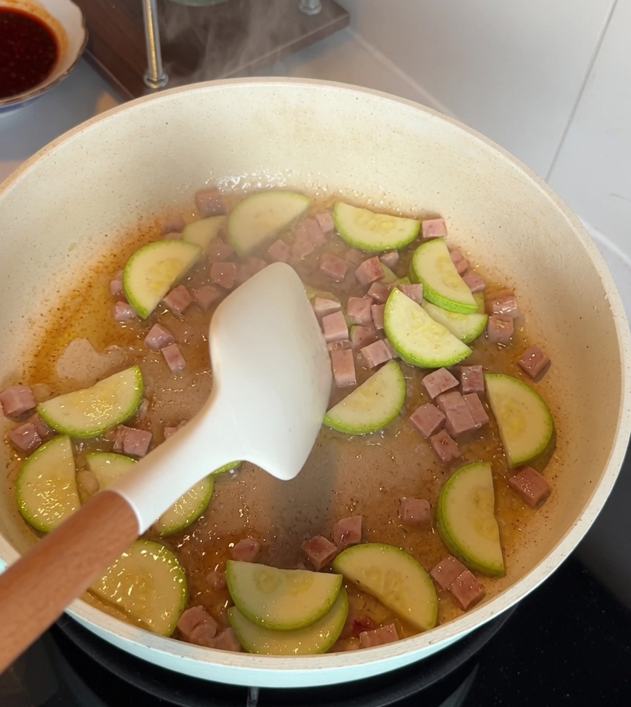 Rodajas de calabacín y cubos de carne de almuerzo salteándose juntos en una sartén antiadherente.