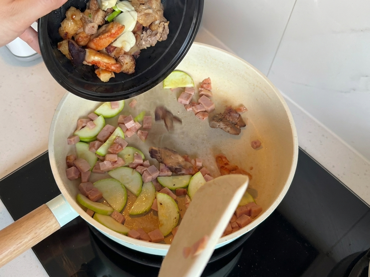 Una sartén conteniendo calabacín salteado y carne de almuerzo con cebolletas, ajo y trozos de carne precocida añadidos.