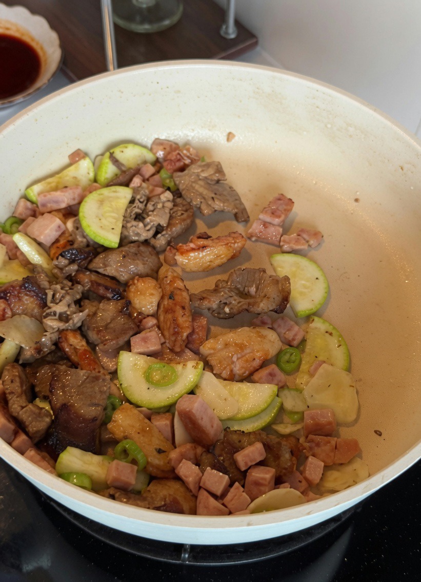 Mezcla de huevo batido siendo revuelta con calabacín y carne de almuerzo en una sartén blanca.