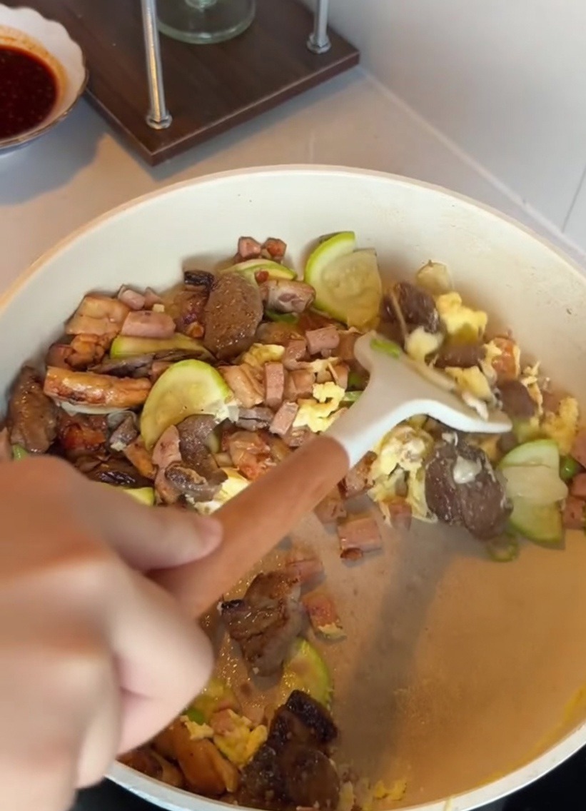 Un tazón de arroz blanco siendo añadido a una sartén con calabacín salteado, carne y huevos.