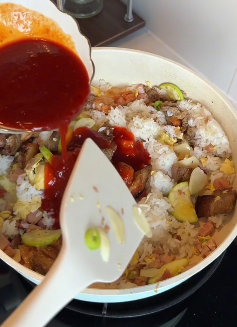 Salsa de bibimbap al estilo coreano vertiéndose sobre el arroz y los ingredientes en una sartén.